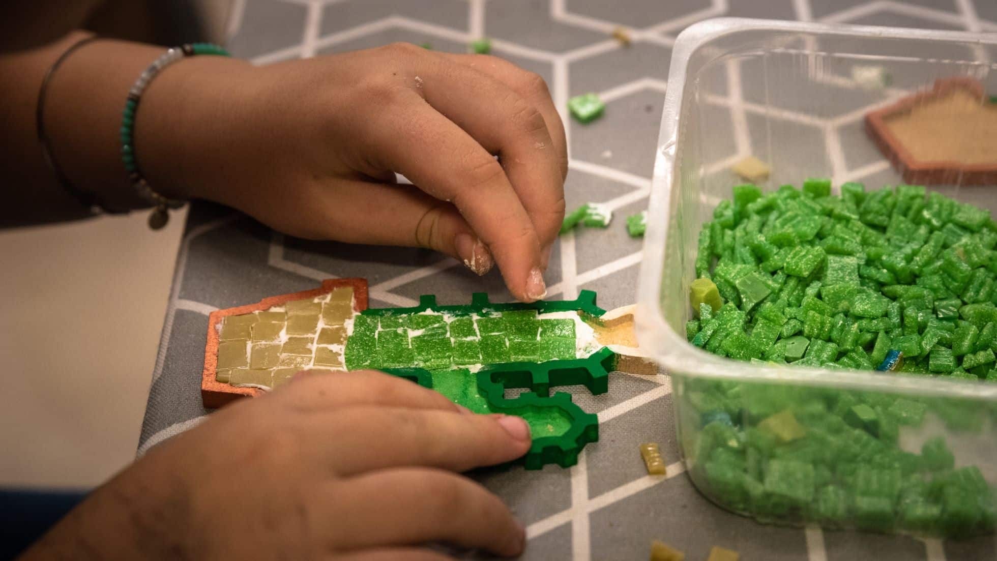 Foto di mani che creano un piccolo mosaico verde.